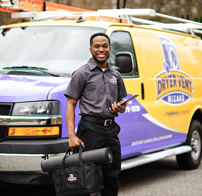 Smiling technician standing beside van holding a tablet.