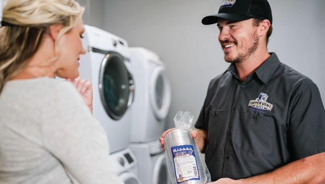 Commercial dryer vent cleaner showing business owner dryer vent hose while standing in front of stacked dryers.