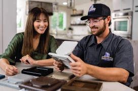 Homeowner and dryer vent cleaning professional review exterior vent cap replacement options while sitting in kitchen.