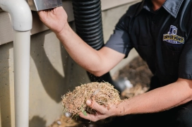 Professional dryer vent cleaner holding a pile of dirt and sticks from cleaning out dryer vent line.